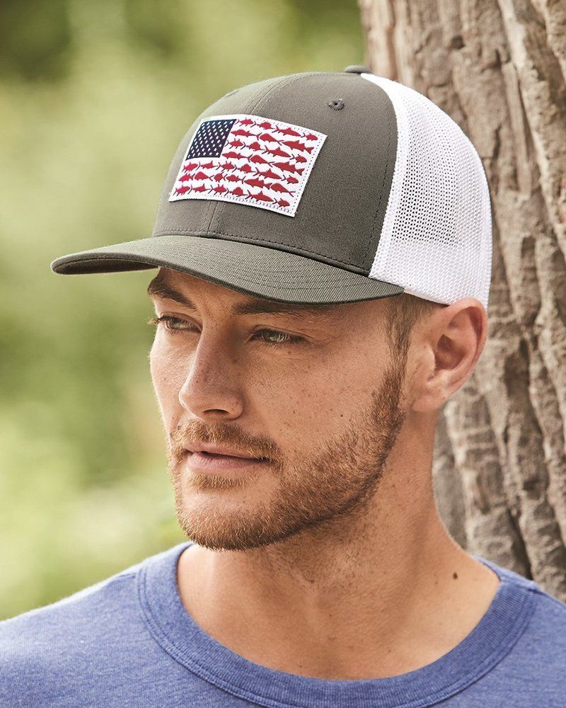 A man wearing a hat with an american flag on it is standing next to a tree.