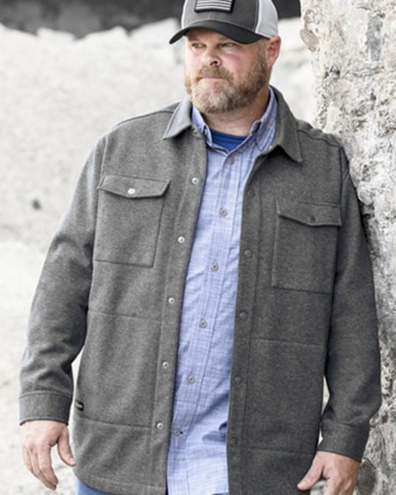 A man wearing a hat and a gray jacket is leaning against a wall.