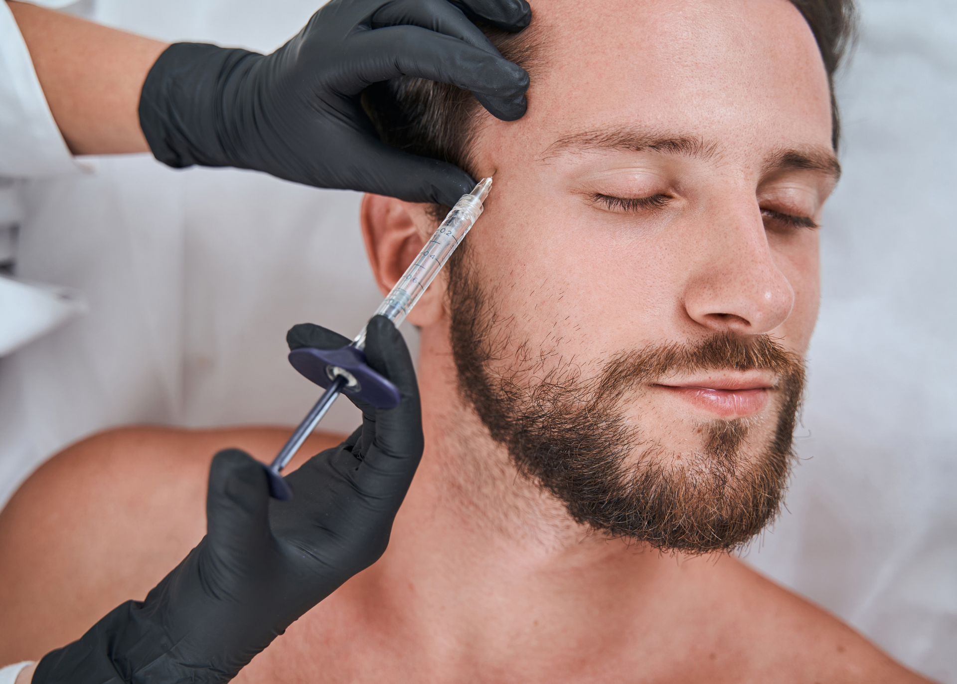 A man with a beard is getting a botox injection in his forehead.