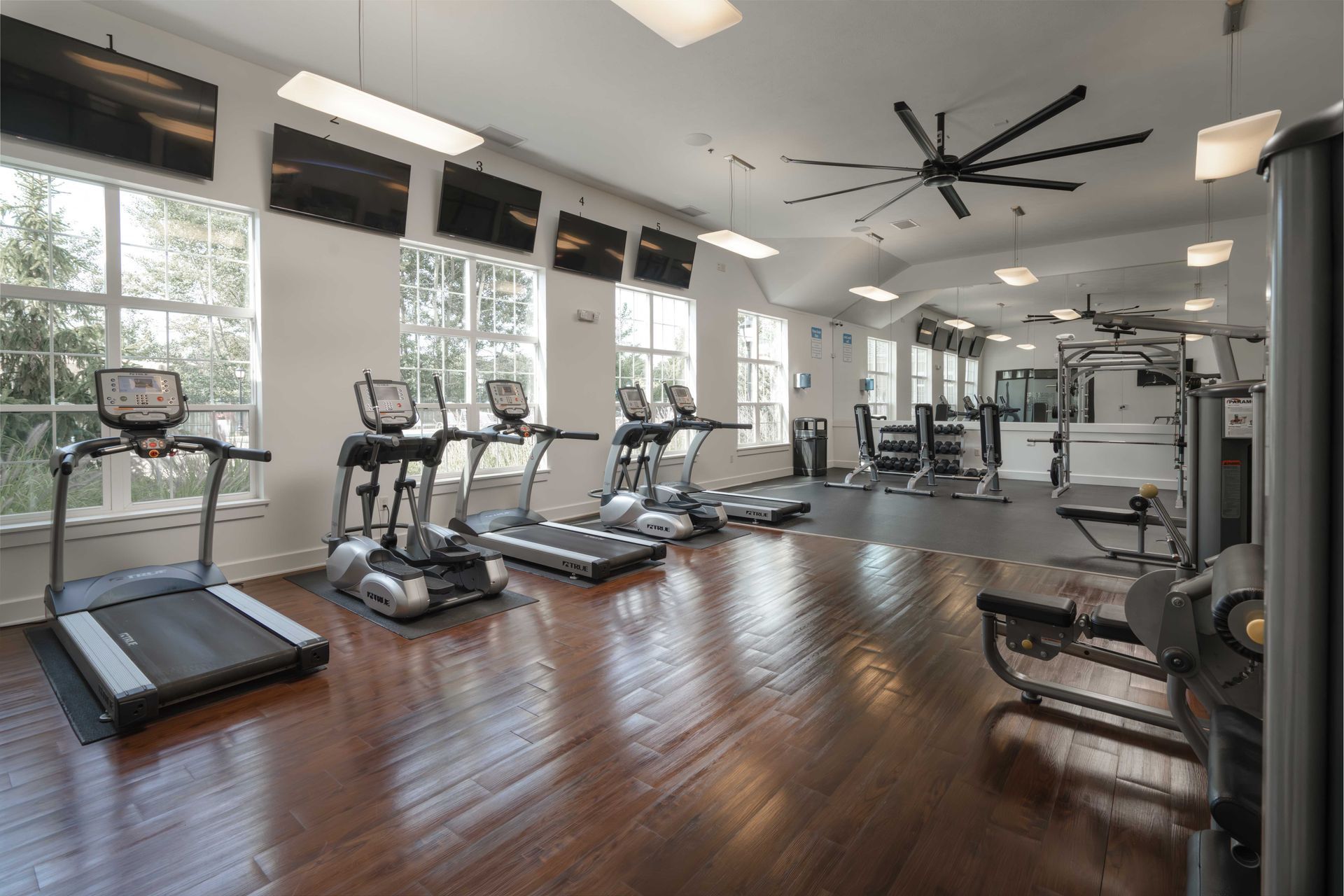Gym with treadmills, elliptical machines, weight machines, and dark wood floor.