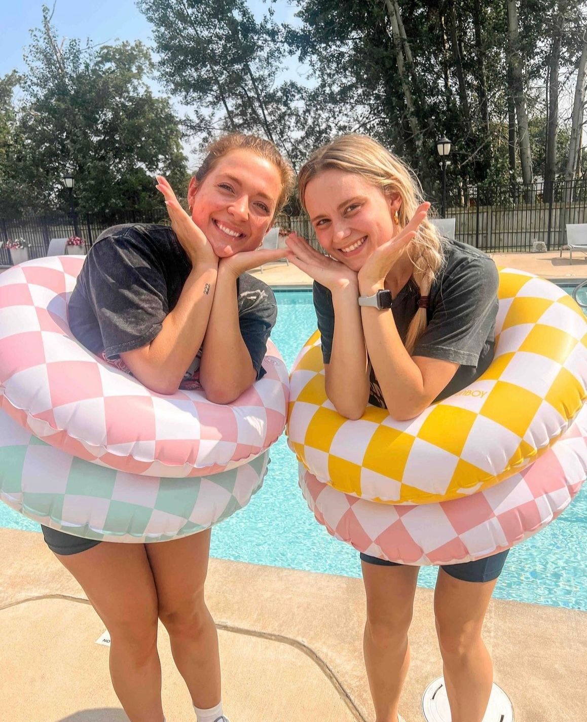 Two women with pool floats standing next to pool.