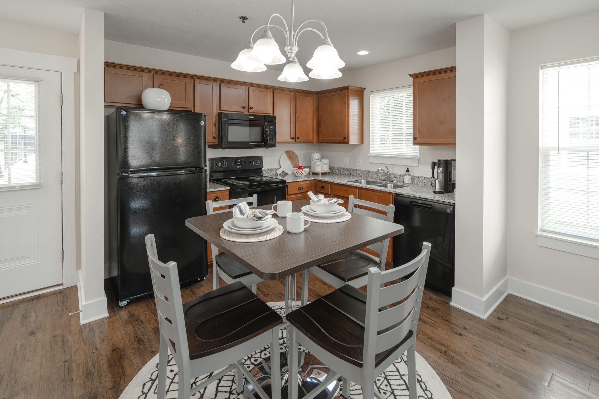 A kitchen with brown cabinets, black appliances, and a table with four chairs.