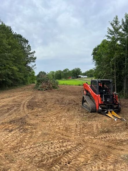 Orange skid steer clearing a dirt lot beside trees under a cloudy sky