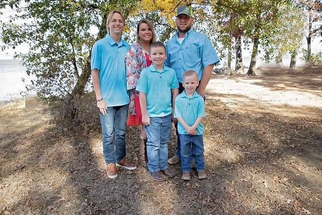 Family of five in a park, posing for a photo; two adults, three children; trees and water in background.