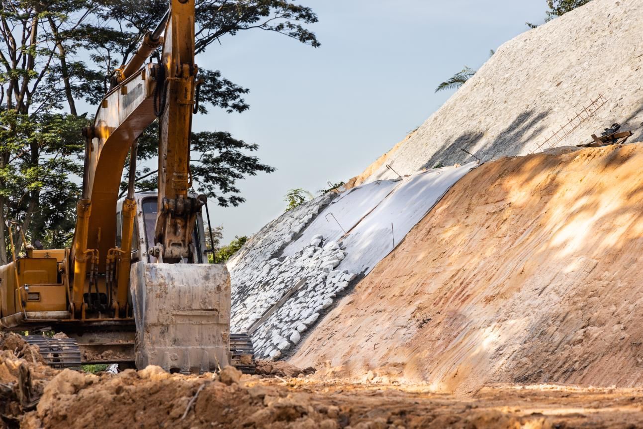 Yellow excavator on a construction site, grading a hillside covered in white material.