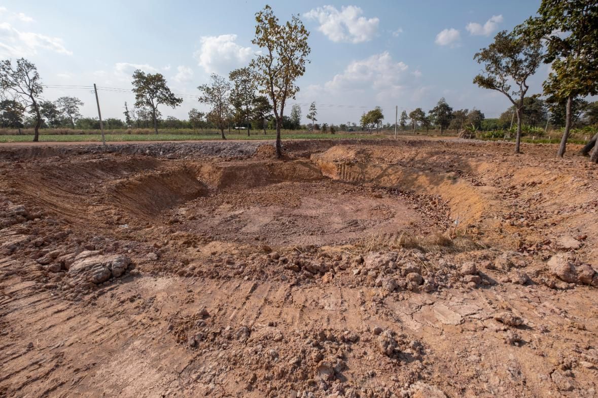 Brown excavation site in a field with trees, under a blue sky.