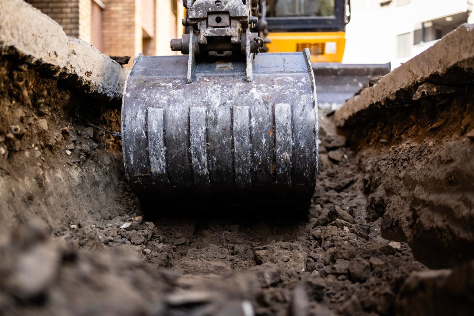 Excavator bucket scooping dirt from a trench on a construction site.