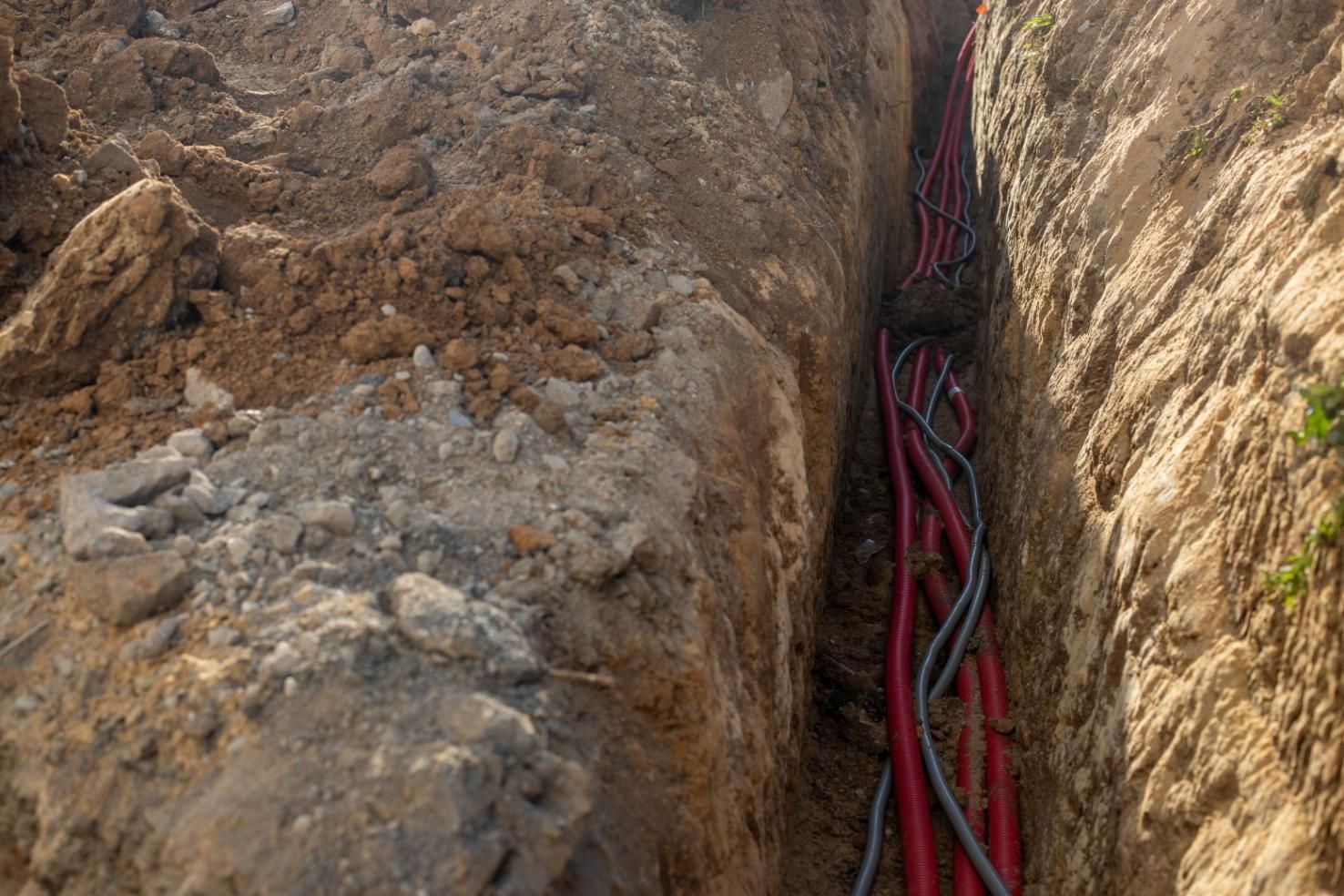 Trench with red and gray electrical cables running through it, surrounded by brown dirt.