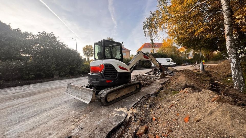 Mini excavator working on road, removing asphalt and debris. 