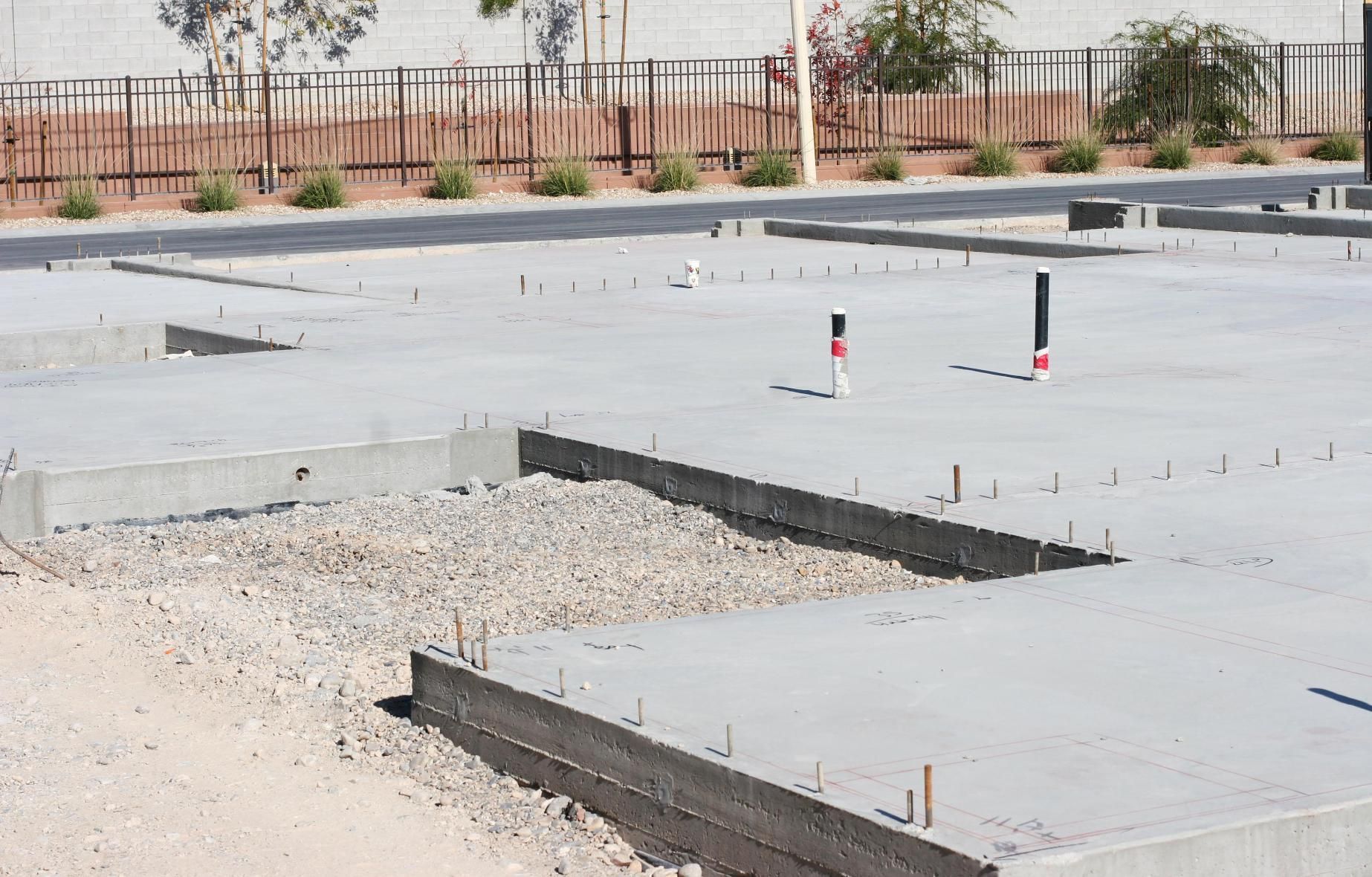 Concrete foundation with gravel, plumbing pipes, and rebar; outdoors, daytime.