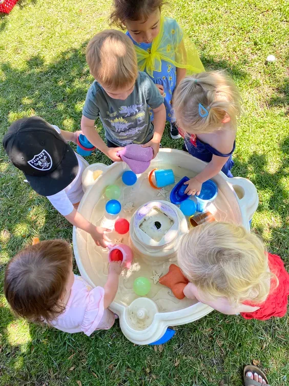 A group of children are playing with a water table in the grass.