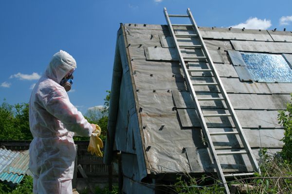 A man in a protective suit is standing next to a ladder on the roof of a house.