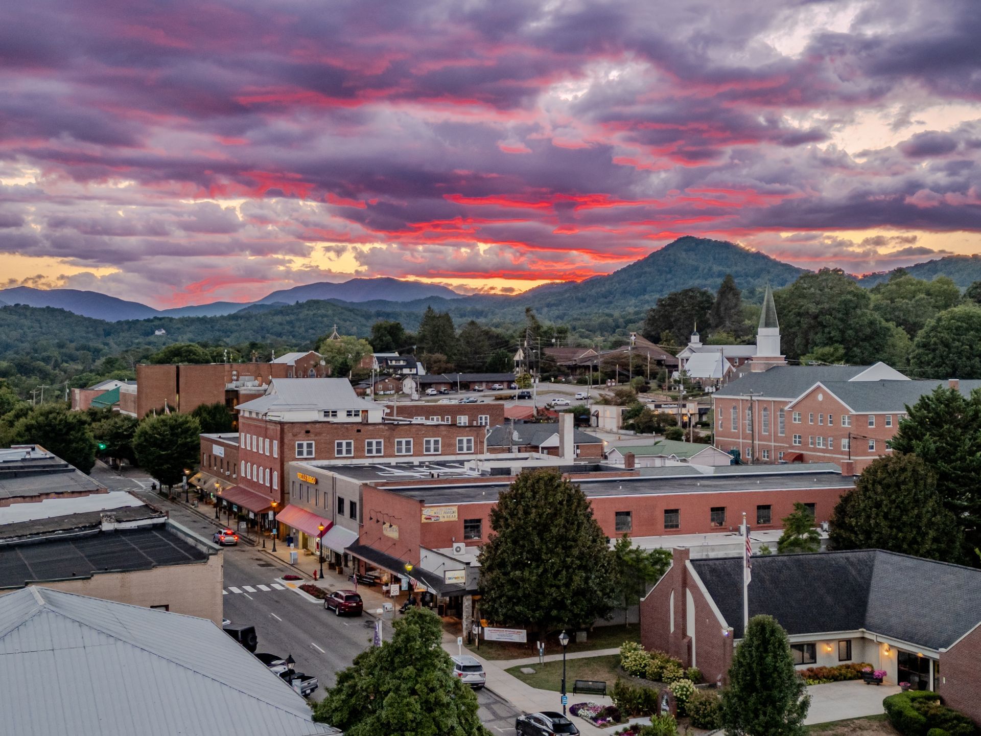 Townscape with buildings and mountains under a colorful sunset sky.
