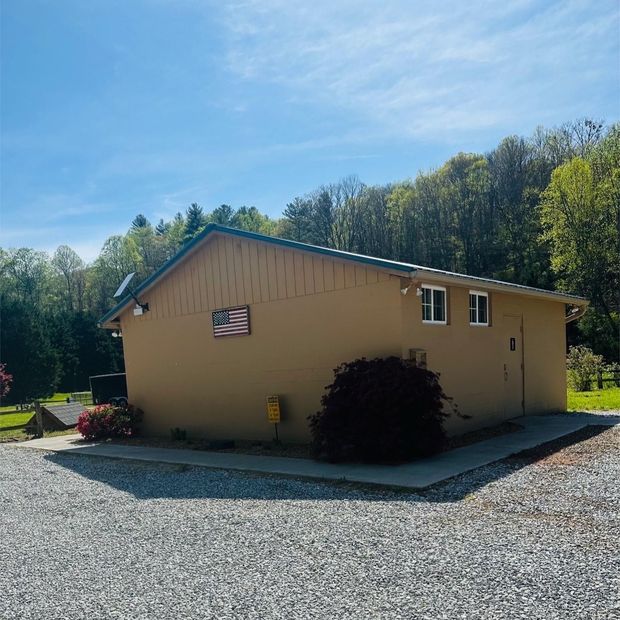 Tan building with an American flag, set in a gravel area with trees and a blue sky.