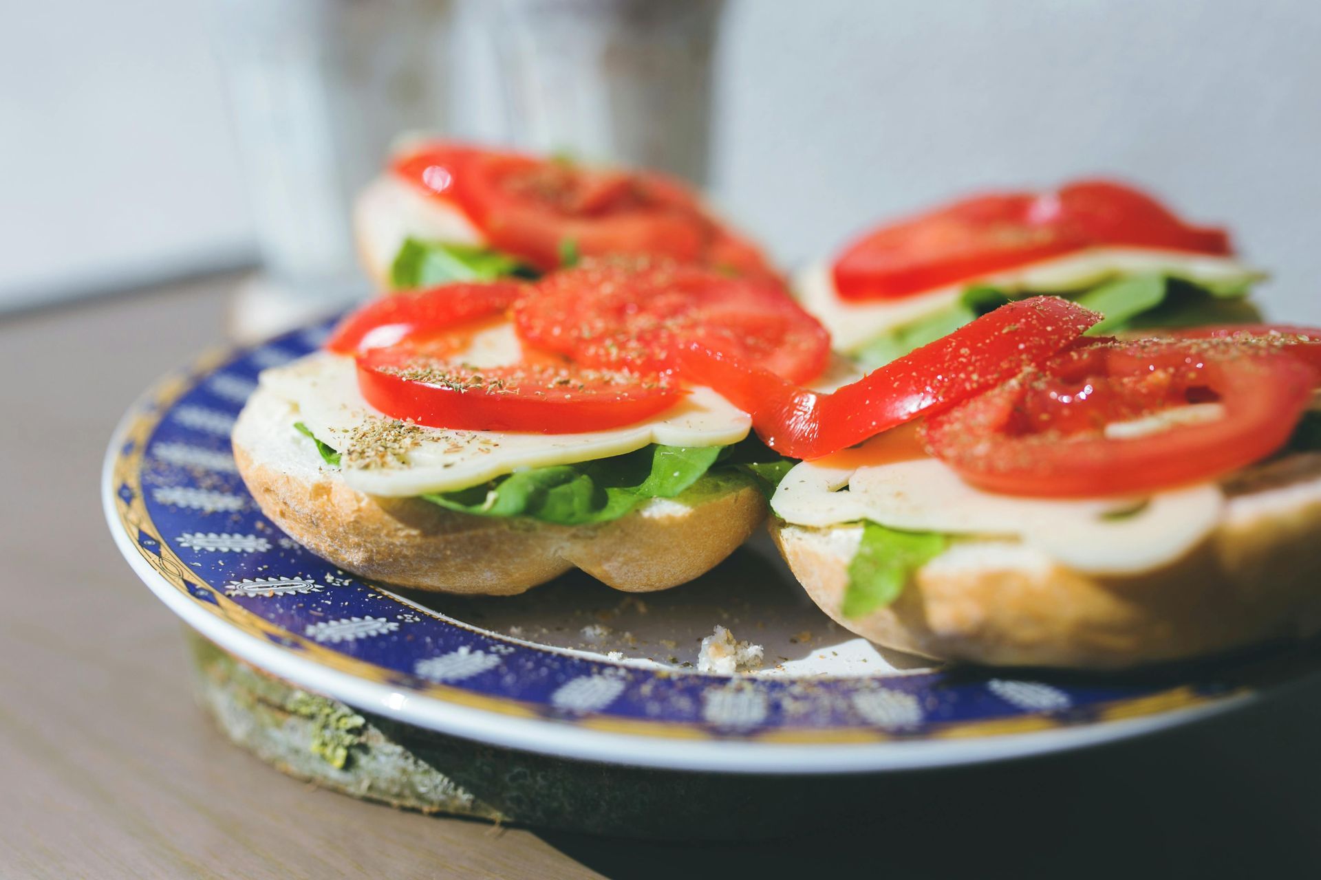 Small sandwiches on a blue patterned plate, topped with tomatoes and seasoning.
