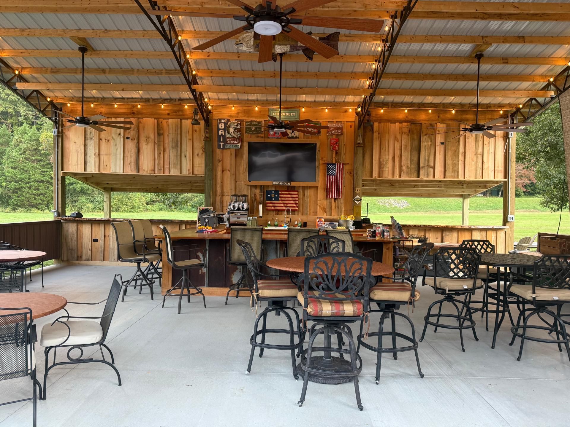 Outdoor bar area with a rustic wood design, seating, and a TV.
