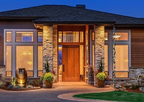 A large house with a wooden door and lots of windows is lit up at night.