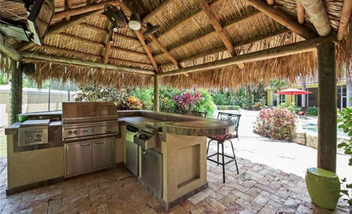 An outdoor kitchen with a thatched roof and stainless steel appliances