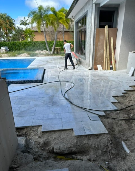 A man is standing on a tiled patio next to a pool.