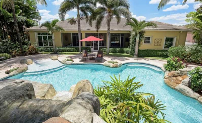 A large swimming pool in front of a house with palm trees