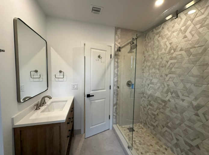 A bathroom with a sink , mirror and walk in shower.