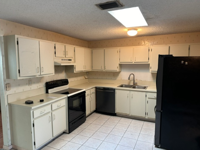 A kitchen with white cabinets and a black refrigerator