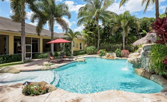 There is a large swimming pool in the backyard of a house surrounded by palm trees.