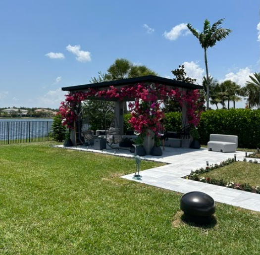 A gazebo with pink flowers is in the middle of a lush green field