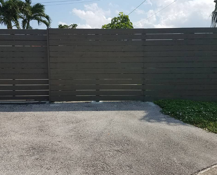 A fence surrounds a driveway with palm trees in the background