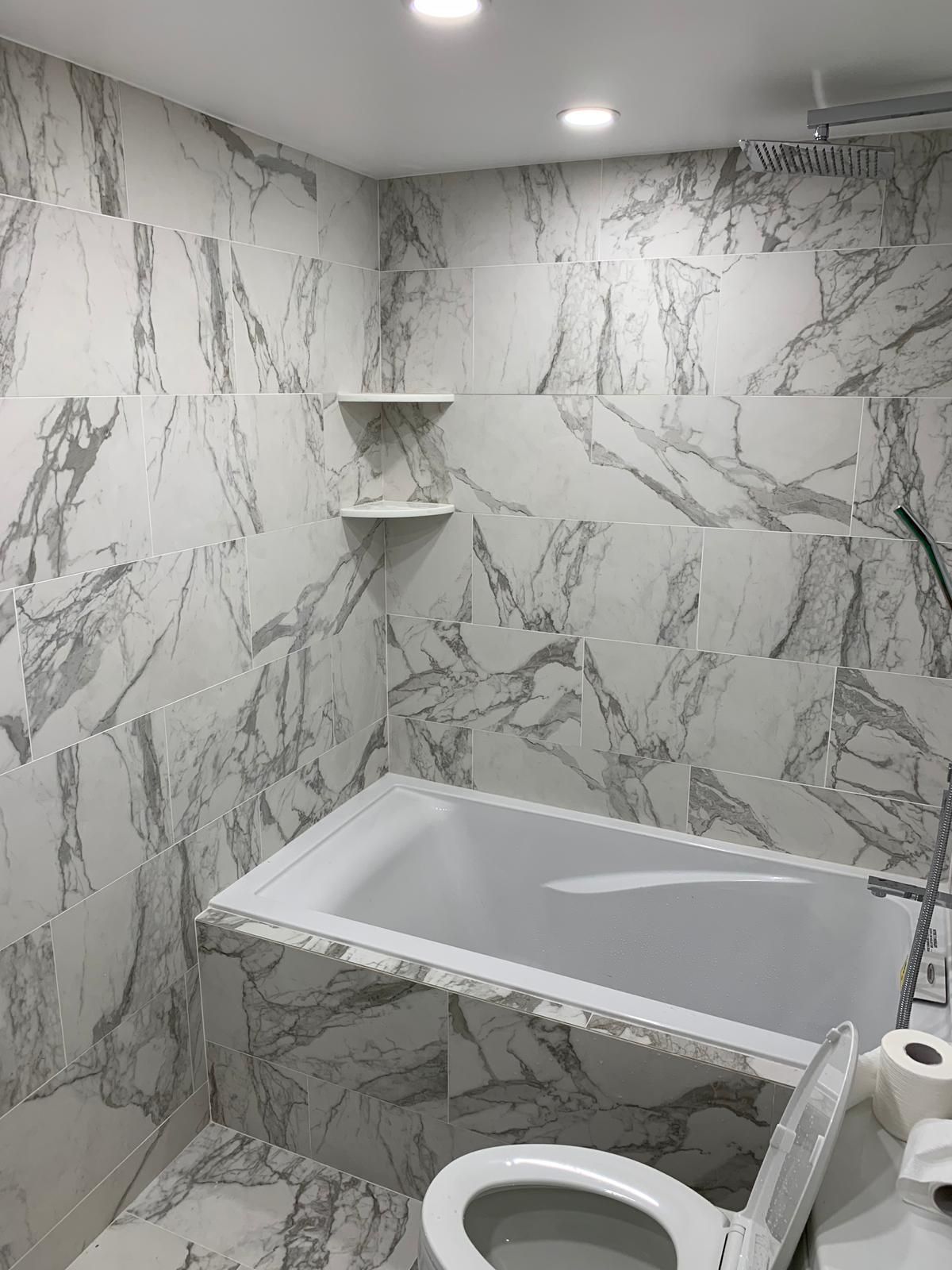 A bathroom with marble tiles , a toilet , and a bathtub.