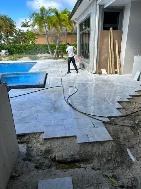 A man is laying tiles on a patio next to a pool.