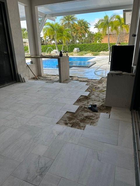A patio with tiles missing and a swimming pool in the background.