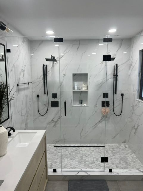Modern bathroom with two glass-enclosed showers, marble tile, black fixtures, and a built-in niche.