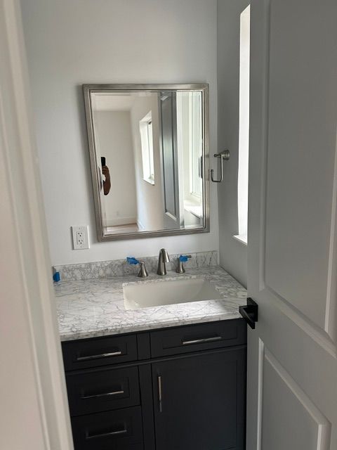 A bathroom with a sink , mirror and window.