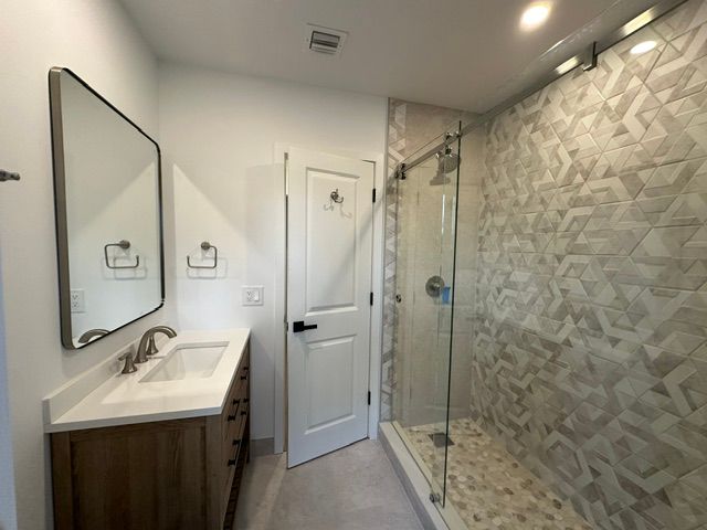 Bathroom with white walls, a wood vanity, a glass shower, and patterned tile.