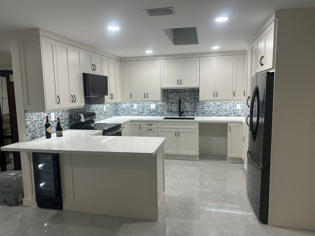 A kitchen with white cabinets and a black refrigerator