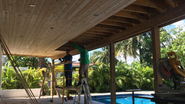 A group of men are working on a wooden structure next to a pool.
