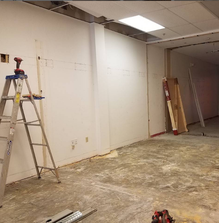 An empty room with a ladder and a drill on the floor.