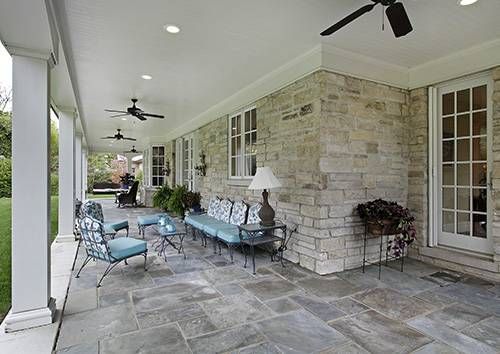 A large stone porch with a couch and chairs and a ceiling fan.