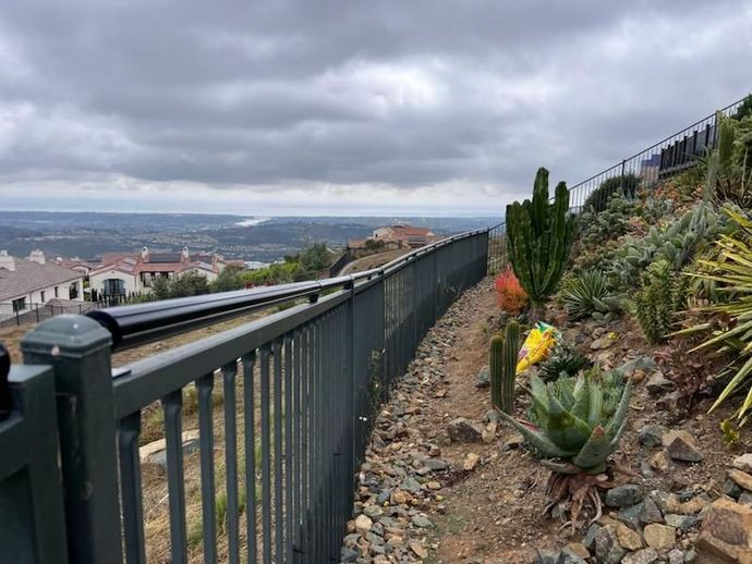 A fence surrounds a rocky hillside with cactus and flowers.