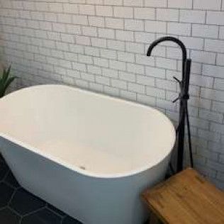 Freestanding white bathtub with black faucet, set against white brick tiles.