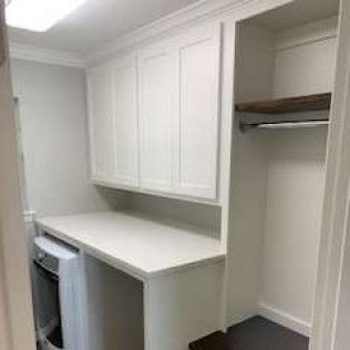 Laundry room with white cabinets, countertop, washer, and a small closet with a hanging rod.