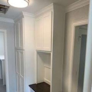 White built-in cabinets with a bench and doorway in a bright hallway.