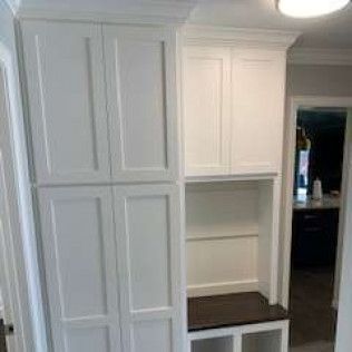 White built-in storage unit with cabinets and open shelf; dark bench below.