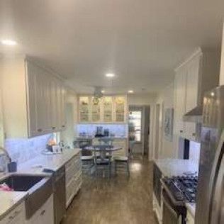 A white kitchen with cabinets, a sink, and a stove, with a table and chairs in the background.