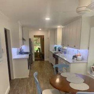 Kitchen with white cabinets, wood floor, round table, chairs.