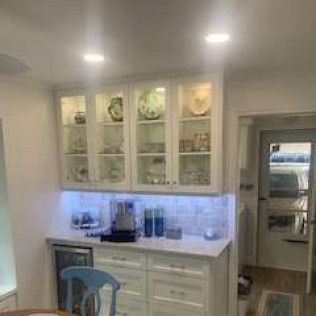 White cabinets with glass doors, illuminated shelf, and a small refrigerator.