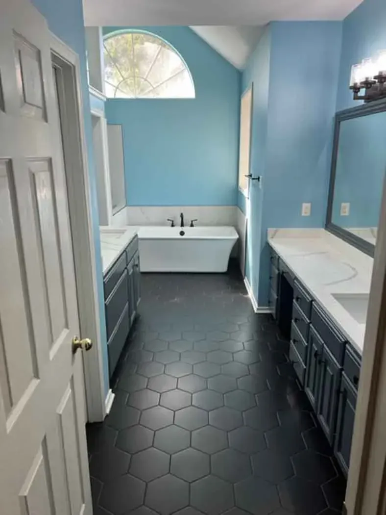 Bathroom with dark hexagon tile floor, blue walls, white bathtub, and double vanity.