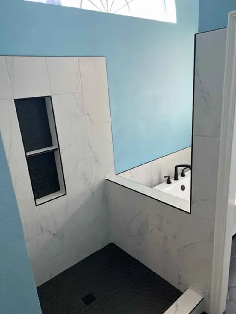 Bathroom shower with white marble-look tiles, black floor, and a blue wall.