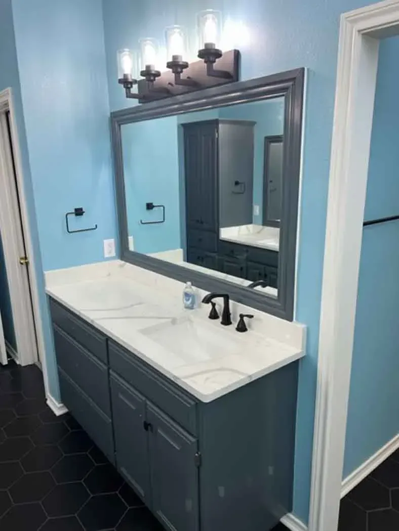 Bathroom with blue walls, gray vanity with white countertop, and large mirror.
